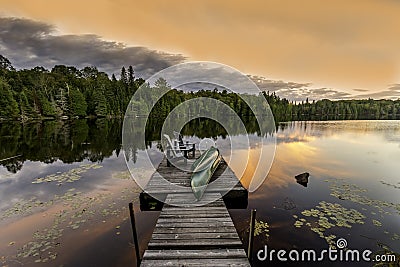 Green Canoe and Chairs on a Dock at Sunset Stock Photo