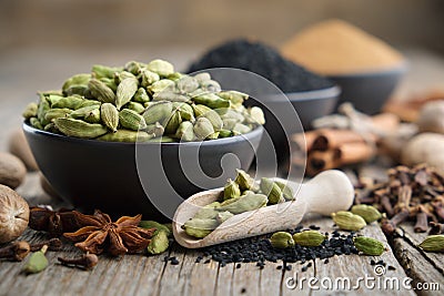 Green cardamom pods in black ceramic bowl in the foreground. Ingredients for cooking. Ayurveda treatments Stock Photo