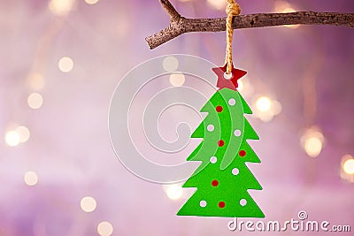 Green Christmas tree with red star ornament hanging on branch. Shining garland golden lights. Purple background. Stock Photo