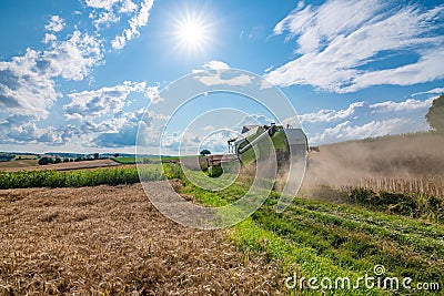 A combine harvester in a field on a sunny, summer day bringing in the harvest. Editorial Stock Photo