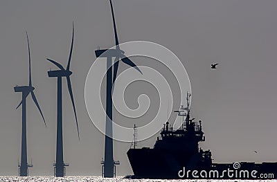 Green energy. Offshore wind farm turbines with ship at sea. Silhouette at dawn. Stock Photo