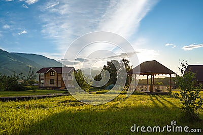 Green grass with cottage, gazebo, touristic tents and mountains on background Stock Photo