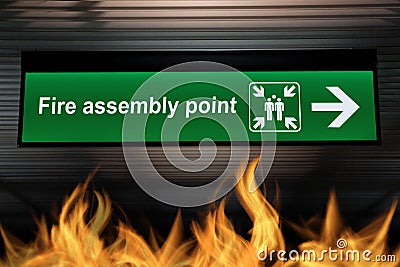 Green fire assembly point sign hanging from ceiling with fire Stock Photo