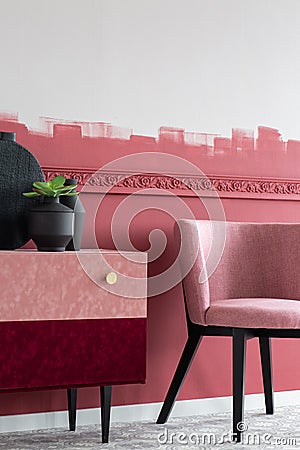 Green flower in black pot nest to black vase on stylish velvet commode next to pastel pink chair Stock Photo