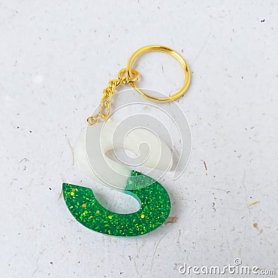 green glitter letters with beads. Golden keychain on white paper background with dried flowers. Top view. Resin craft Stock Photo