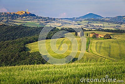 Green grain fields with Vitaleta chapel and Pienza, Tuscany, Italy Stock Photo
