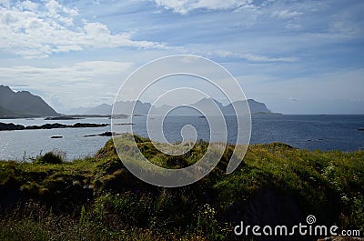 Green grass in front of blue ocean and mighty mountains Stock Photo