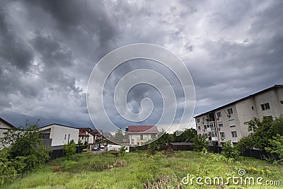 Green grass and houses under dark sky with clouds before storm Stock Photo