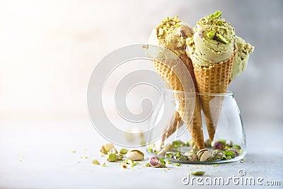 Green ice cream in waffle cone with chocolate and pistachio nuts on grey stone background. Summer food concept, copy Stock Photo