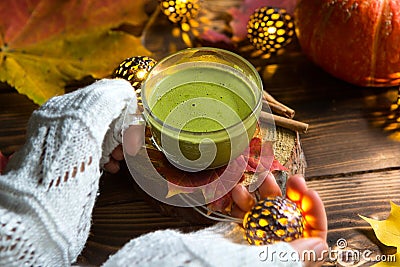 Green Japanese matcha tea with foam in transparent Cup on wooden table in autumn still life. Women`s hand with long white sweater Stock Photo