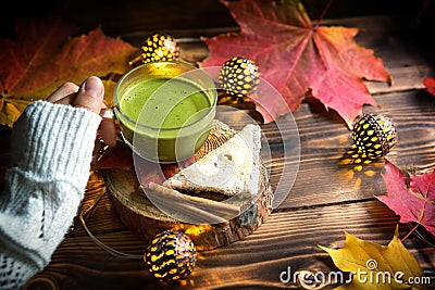 Green Japanese matcha tea with foam in transparent Cup on wooden table in autumn still life. Women`s hand with long white sweater Stock Photo