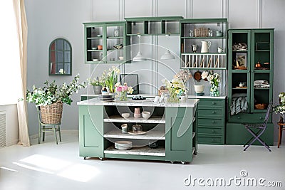 Green kitchen interior with furniture. Stylish cuisine with flowers in vase. Wooden kitchen in spring decor. Cozy home decor. Kitc Stock Photo