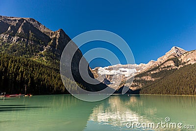 Green lake surrounded by mountains and glaciers in a blue sky day in Banff National Park in Canada Stock Photo
