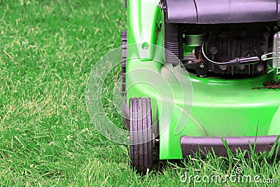 A green lawnmower in the garden. A lawn mower on the green grass. Gardening Stock Photo