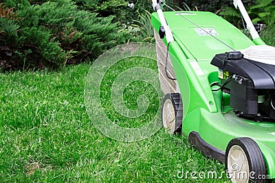 A green lawnmower in the garden. A lawn mower on the green grass. Gardening Stock Photo