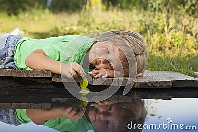 Green leaf-ship in children hand in water, boy in park play with boat in river Stock Photo