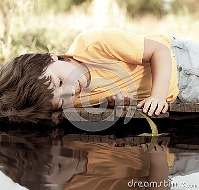 Green leaf-ship in children hand in water, boy in park play with boat in river Stock Photo