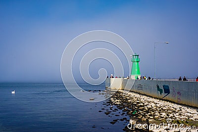 Green lighthouse, fog and blue water in contrasting sunlight Editorial Stock Photo