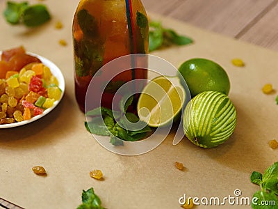Green lime, leaves of mint, a bottle of cocktail and a plate with raisins and dried apricots on a blurred background. Stock Photo