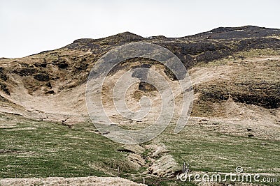 A green meadow with a furrow for the gathering of mountain water, with green grass. Against the backdrop of a hill with Stock Photo