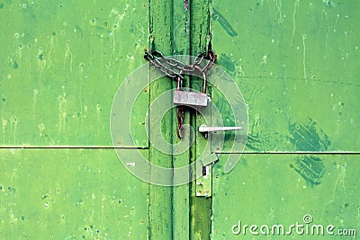 Green metal doors with cracked paint and dilapidated door handle locked with rusted chain and old padlock Stock Photo
