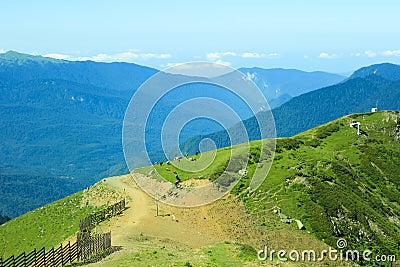 A green mountain range against the background of distant mountain peaks with a fence and a herd of cows in the foreground Stock Photo