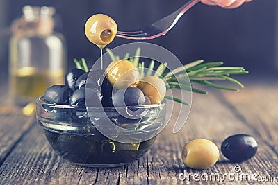 Green olives in a bowl and fork with drops of olive oil on a dark rustic wooden background. Olives on olive wood Stock Photo