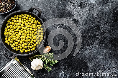 Green peas in a cast-iron bowl. Canned food. Black background. Top view. Copy space Stock Photo