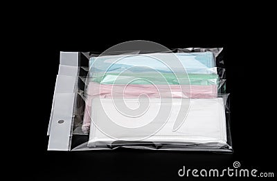 Green, pink, light blue and white ear loop disposable face mask in plastic bag overlapping, used for covering mouth and nose. Stock Photo