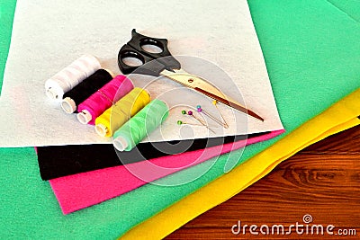 Green, pink, yellow, white and black felt sheets. Scissors, thread and pins on a wooden table Stock Photo