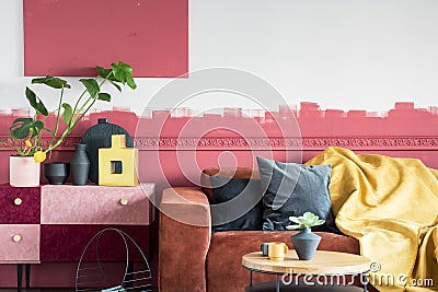 Green plant in white pot next to black and gold vases on pastel pink and burgundy shelf in living room with ombre wall and brown Stock Photo