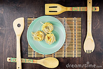 Green plate with fettuccine paste on a bamboo napkin and wooden spatulas on a mahogany background Stock Photo