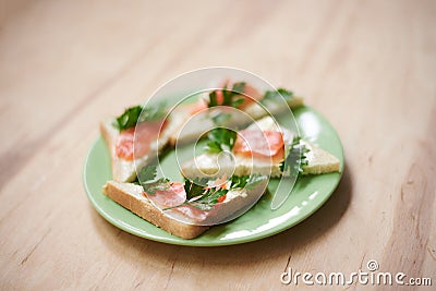 Green plate with salmon sandwiches with butter and parsley on wooden table. Buffet breakfast lunch meal. Healthy eating. Fish diet Stock Photo