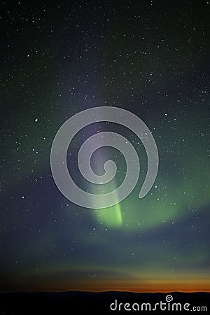 Green-purple streak of aurora over twilight horizon. Many stars Stock Photo