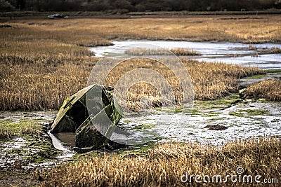 A green row boat sunk in water at a marsh on the Kent coast Stock Photo