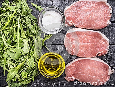 Green salad of arugula with oil and salt with raw pork steak wooden rustic background top view close up Stock Photo