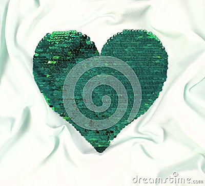 Green sequins heart shape embroidered on white textile wavy folds background. Valentines day luxury and glamour greeting card Stock Photo