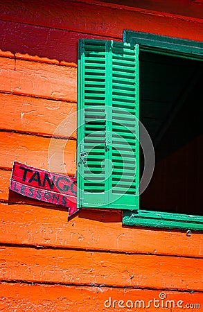 Green shuttered window with orange walls is backdrop for Tango lesson sign in La Boca Stock Photo
