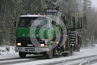 Green SISU Truck Hauls John Deere Forwarder in Winter Editorial Stock Photo