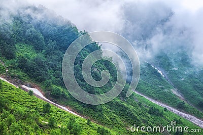 The green slopes of high mountains are hidden in clouds and fog. Melting snow in high mountains in summer Stock Photo