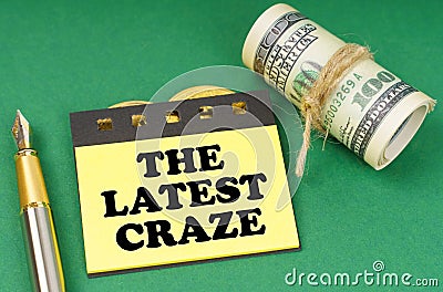 On a green surface are a pen, dollars and yellow stickers with the inscription - The Latest Craze Stock Photo