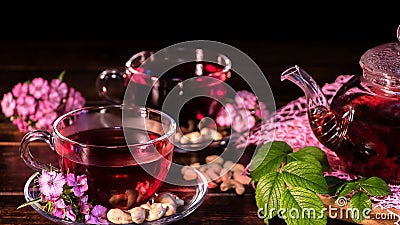 Green tea leaves or leaves of medicinal herbs lie on the table with a teapot and mugs of red tea, cashew nuts and clove flowers. Stock Photo