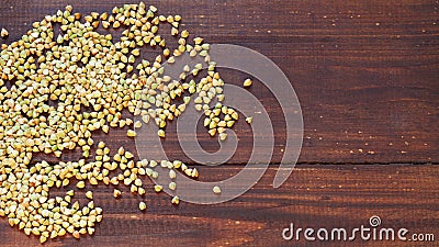 Green unroasted buckwheat grits are poured on a brown wooden surface. Copy space Stock Photo