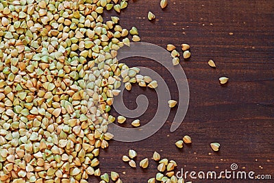 Green unroasted buckwheat grits are poured on a brown wooden surface. Copy space Stock Photo