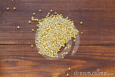 Green unroasted buckwheat is poured on a brown wooden table in a small pile Stock Photo