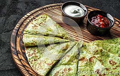 Green vegan crepes with spinach on plate served with cream or gem on dark background, close up view. Pancake week or Shrovetide. Stock Photo