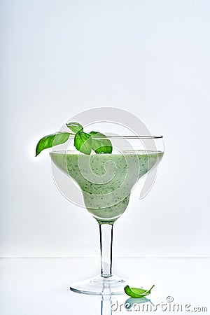 Green vegetable juice or smoothie garnished with leaf of fresh basil in coctail margarita glass isolated on white Stock Photo