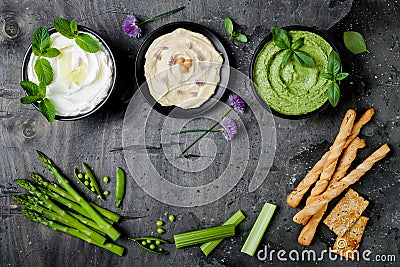 Green vegetables raw snack board with various dips. Yogurt sauce or labneh, hummus, herb hummus or pesto with crackers, grissini Stock Photo