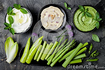 Green vegetables raw snack board with various dips. Yogurt sauce or labneh, hummus, herb hummus or pesto with fresh vegetables. Stock Photo