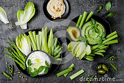 Green vegetables snack board with various dips. Yogurt sauce or labneh, hummus, herb hummus or pesto with fresh vegetables. Stock Photo